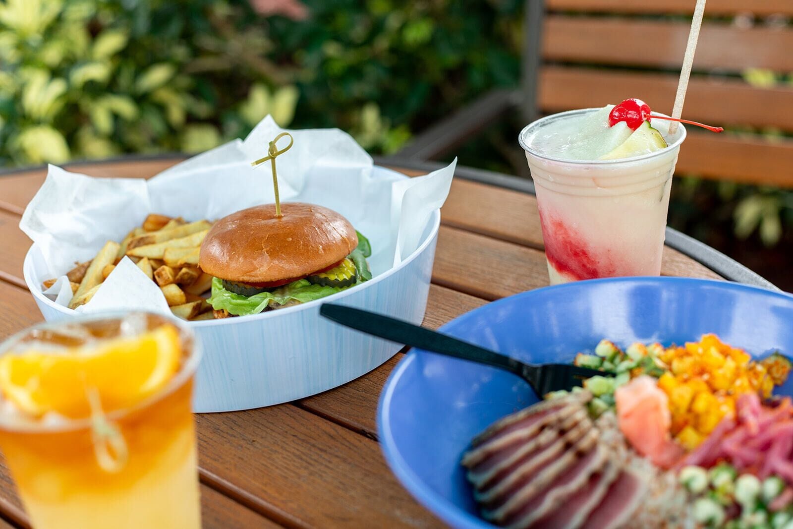 Un repas composé d’un hamburger, de frites, d’une salade et d’une boisson, servi sur une table en bois.