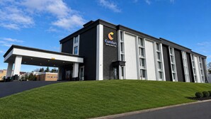 Ein modernes Hotelgebäude mit flachem Dach, einer überdachten Eingangsparte und einem gepflegten Rasen davor.