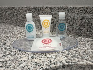Tre hygienprodukter på en bänkskiva av granit: ett återfuktande balsam med doft av citrus och mynta, en fuktgivande lotion för kroppen med doft av citrus och mynta samt ett uppfriskande schampo med doft av citrus och mynta.