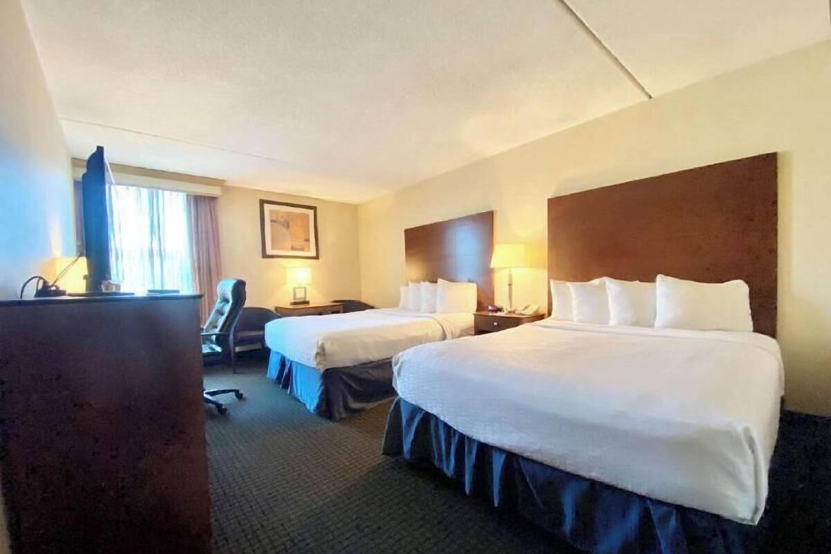 Habitación de hotel con dos camas, un escritorio, una silla, una lámpara y un cuadro en la pared.