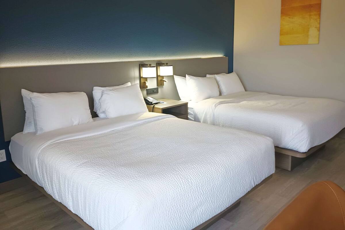 Una habitación de hotel con dos camas, una mesita de noche y una lámpara de pared.