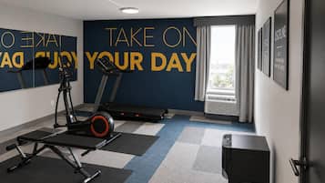 A gym with exercise equipment, motivational wall text, and a window with curtains.