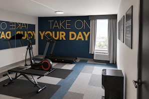 Una palestra con attrezzature per esercizi, scritte motivazionali al muro e una finestra con tende.