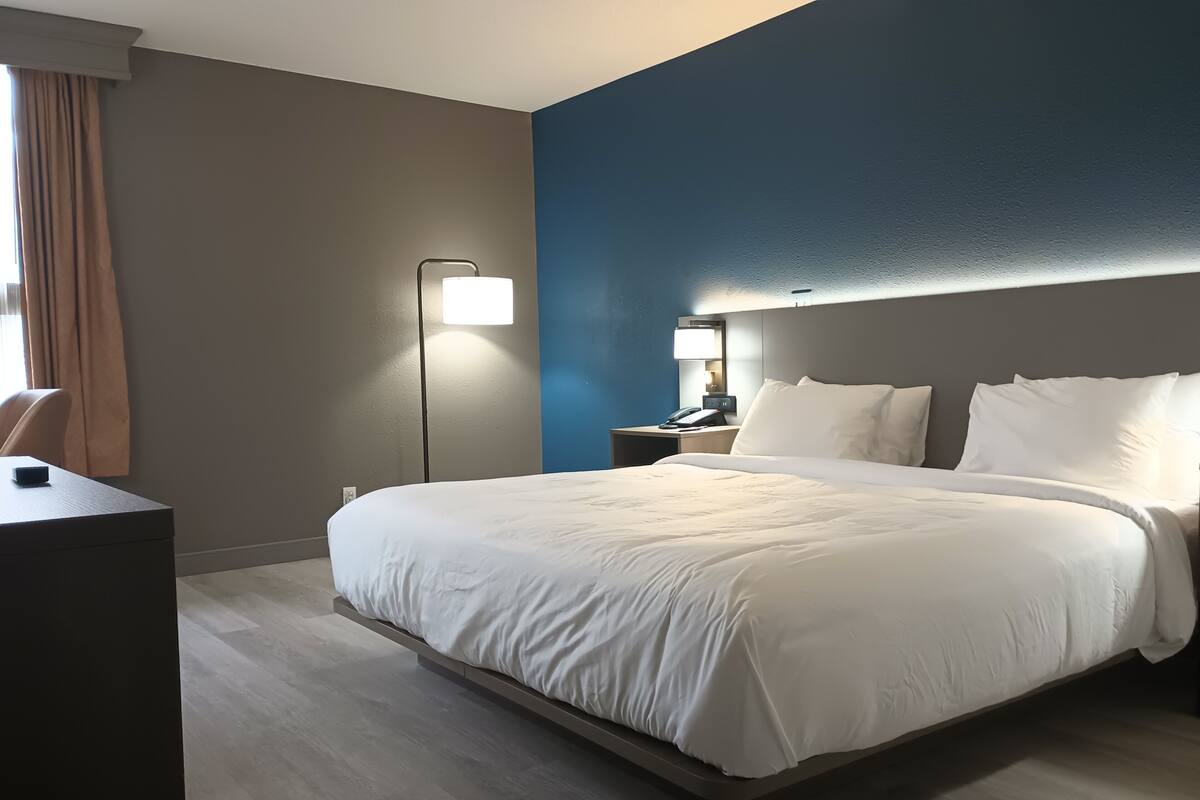 Una habitación de hotel con una cama grande, un escritorio y una mesita de noche con lámpara.