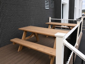 Une terrasse en bois avec des tables de pique-nique et une rambarde.