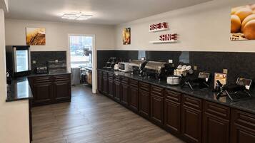 Una cocina moderna con armarios de madera oscura, encimera negra y diversos electrodomésticos, incluyendo un microondas, cafetera y una vitrina para alimentos.