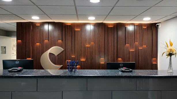 Ein Empfangsschalter mit zwei Dell-Computern, eine große Holzwand mit einem Halbmondmuster und eine Vase mit Blumen.