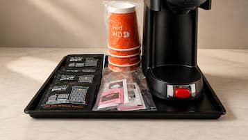 Una cafetera, una pila de cápsulas de café naranja y una bandeja con cápsulas de café y una revista.