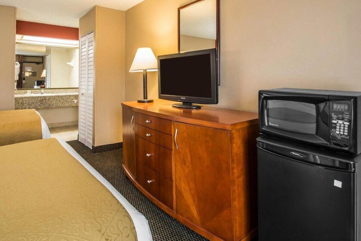 A hotel room with a bed, a wooden dresser, a television, a microwave, and a mirror.