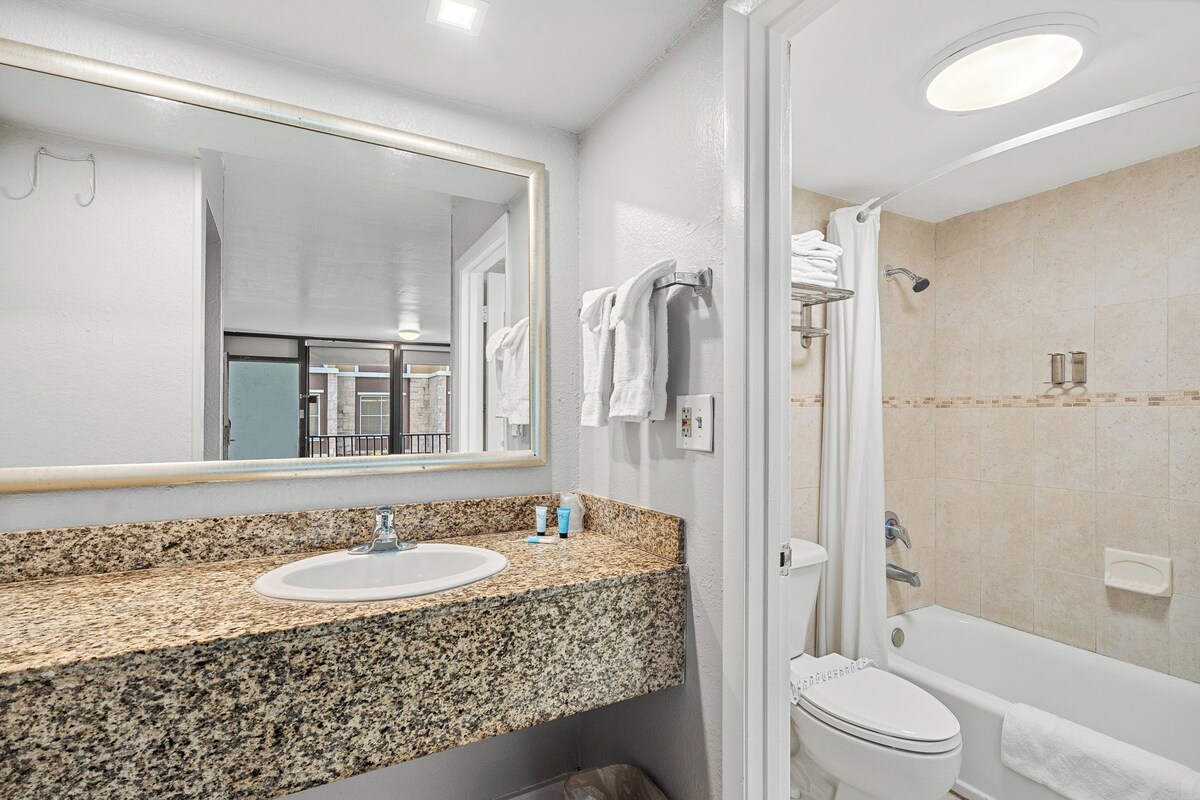A bathroom with a granite countertop sink, a large mirror, a toilet, and a bathtub.