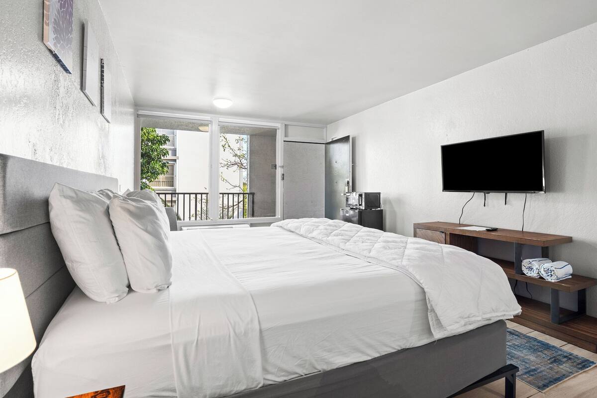Une chambre d’hôtel moderne dotée d’un grand lit, d’une télévision à écran plat, d’un bureau et d’un balcon offrant une vue sur la ville.