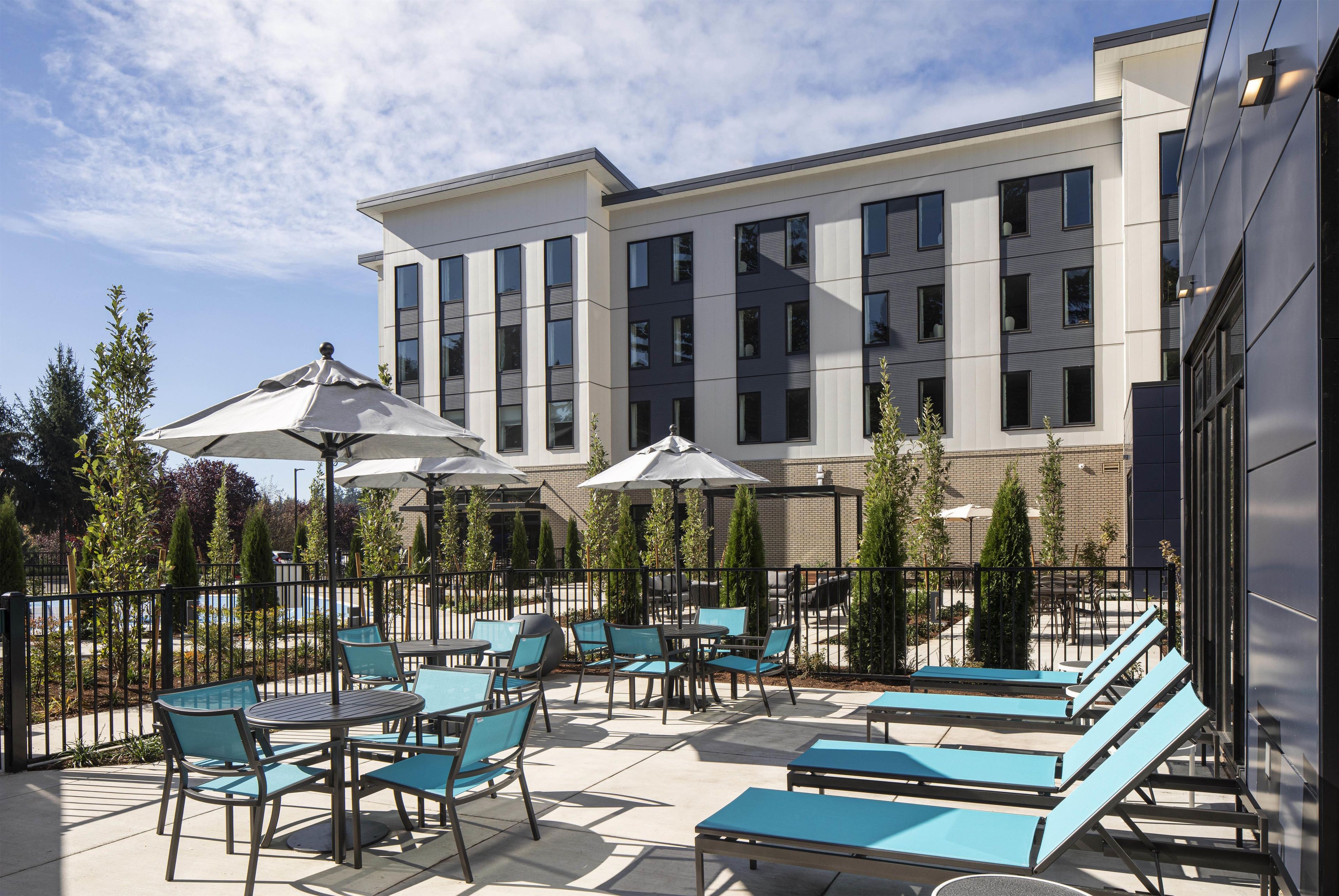 An outdoor patio with tables and chairs, umbrellas, and a building in the background.