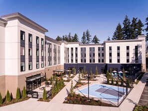 A modern building with multiple windows, a courtyard with outdoor seating, and a basketball court.