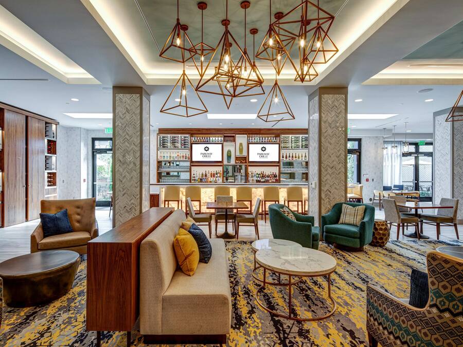 A modern hotel lobby with a bar area, seating arrangements, and a patterned carpet.