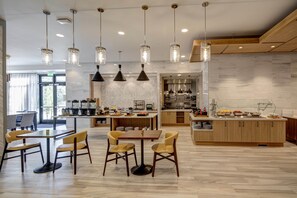 Una cocina moderna con una isla central, iluminación colgante y un comedor con sillas.