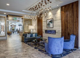 Un moderno vestíbulo de hotel con sofá, sillones, comedor y una original lámpara de araña geométrica.