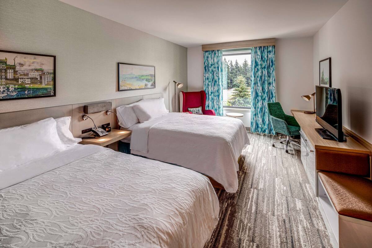 A hotel room with two beds, a desk with a computer, a chair, and a TV.