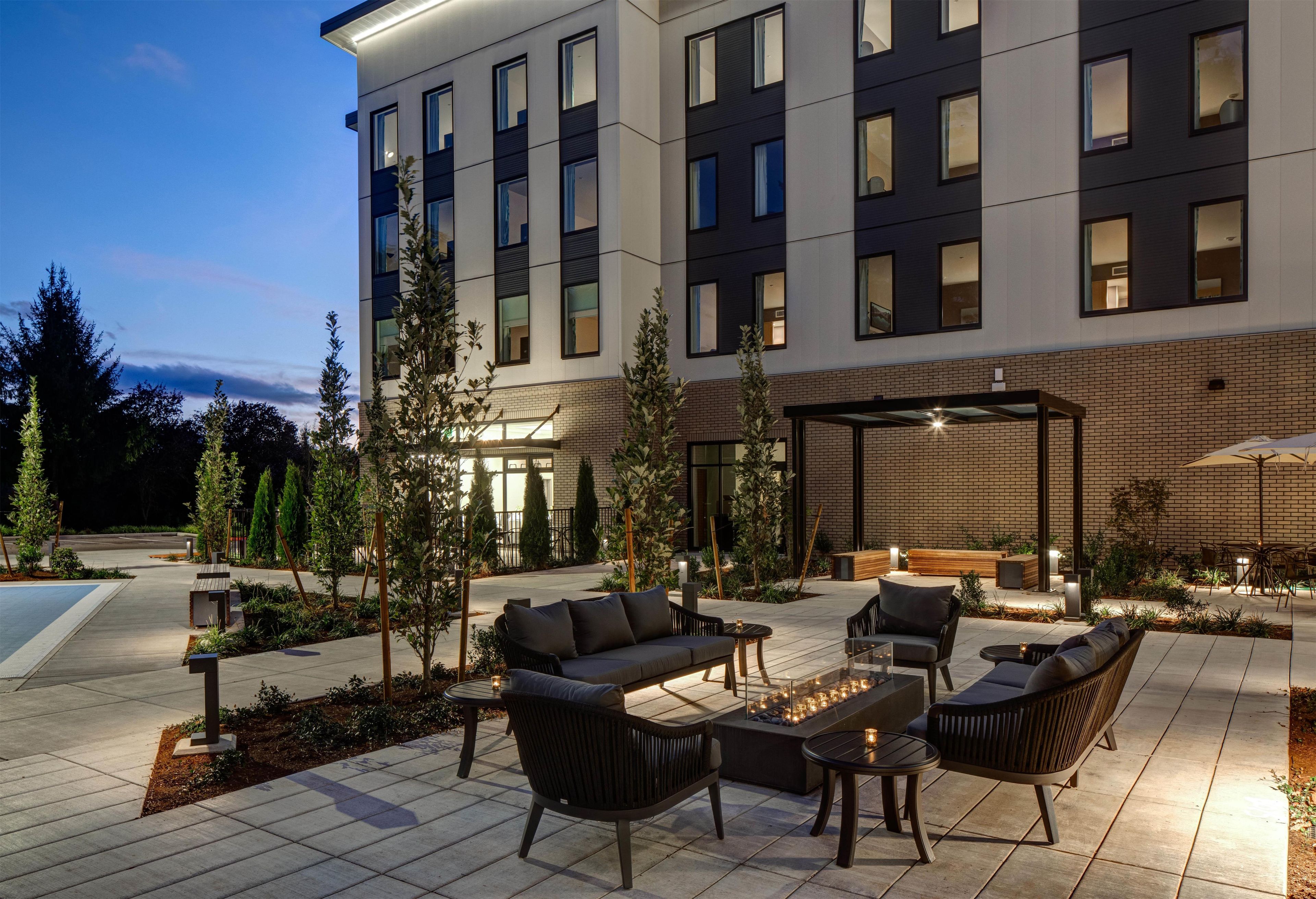 Un espace extérieur moderne, aménagé avec des canapés et des tables, entouré d’un jardin paysager agrémenté d’arbres et d’une piscine.