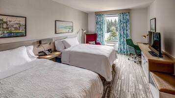 A hotel room with two beds, a desk with a computer, a TV, and a window with curtains.