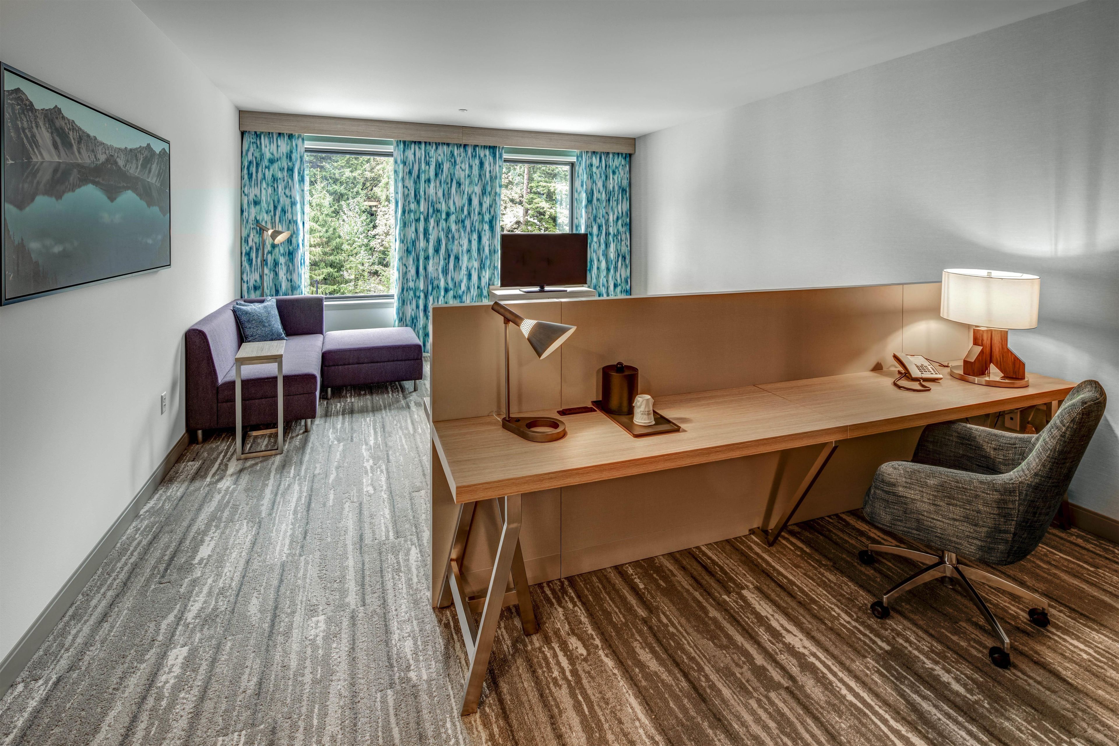 Une chambre d’hôtel équipée d’un bureau, d’une chaise, d’un canapé et d’une grande fenêtre avec des rideaux.