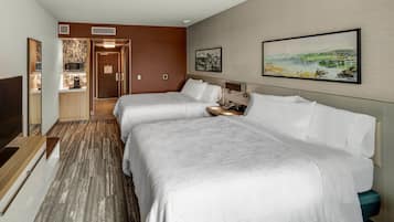 A hotel room with two beds, a wooden floor, a painting on the wall, and a view of the city.