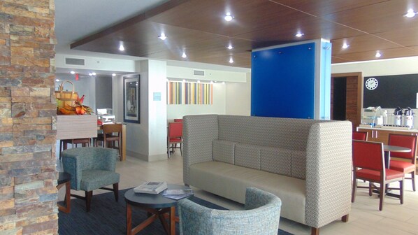 A modern lounge area with a sofa, chairs, a small table, and a kitchen area in the background.