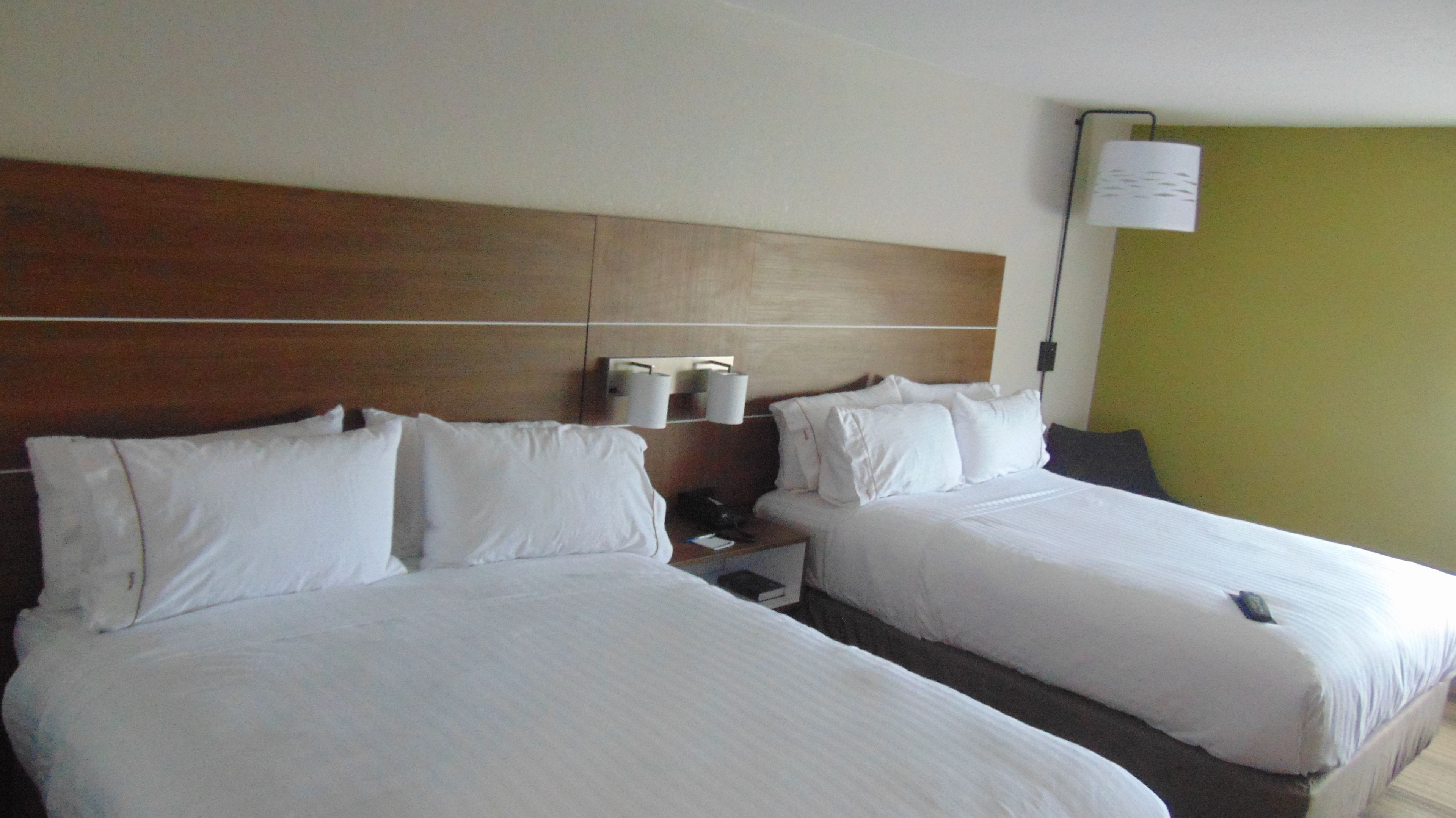 Une chambre d’hôtel avec deux lits, une tête de lit en bois, des lampes de chevet et un mur vert.