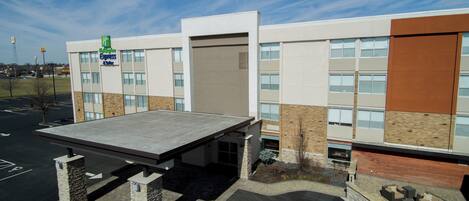 A modern hotel with a covered parking area, a landscaped front, and a clear sky.