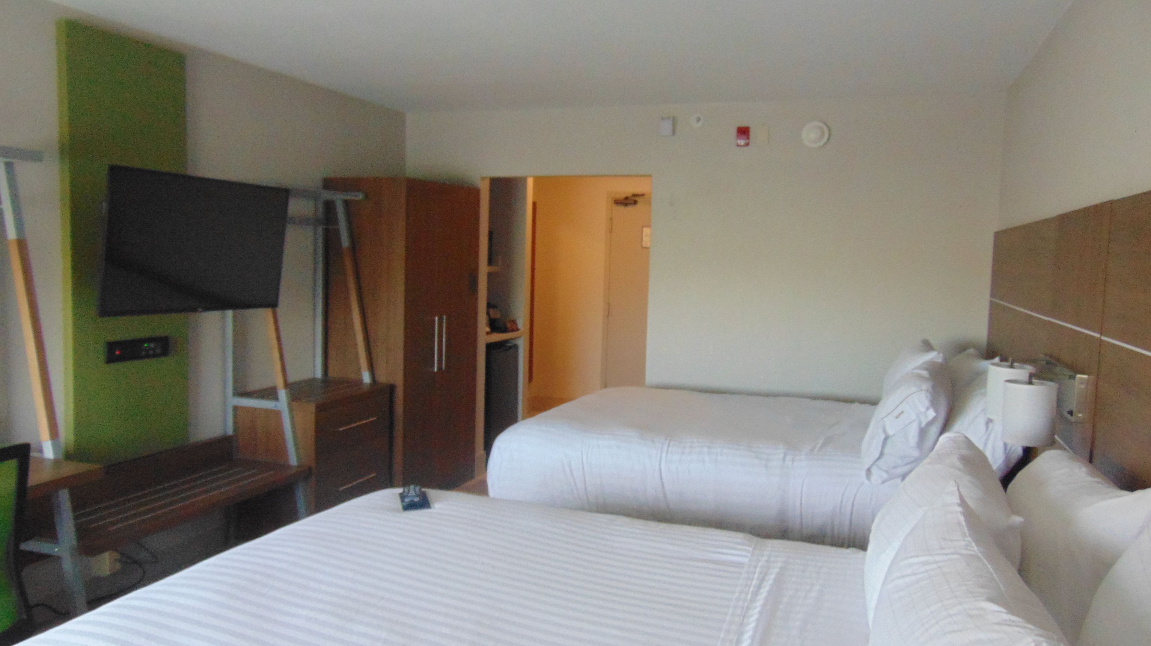A hotel room with two beds, a TV mounted on the wall, a wardrobe, and a small desk.