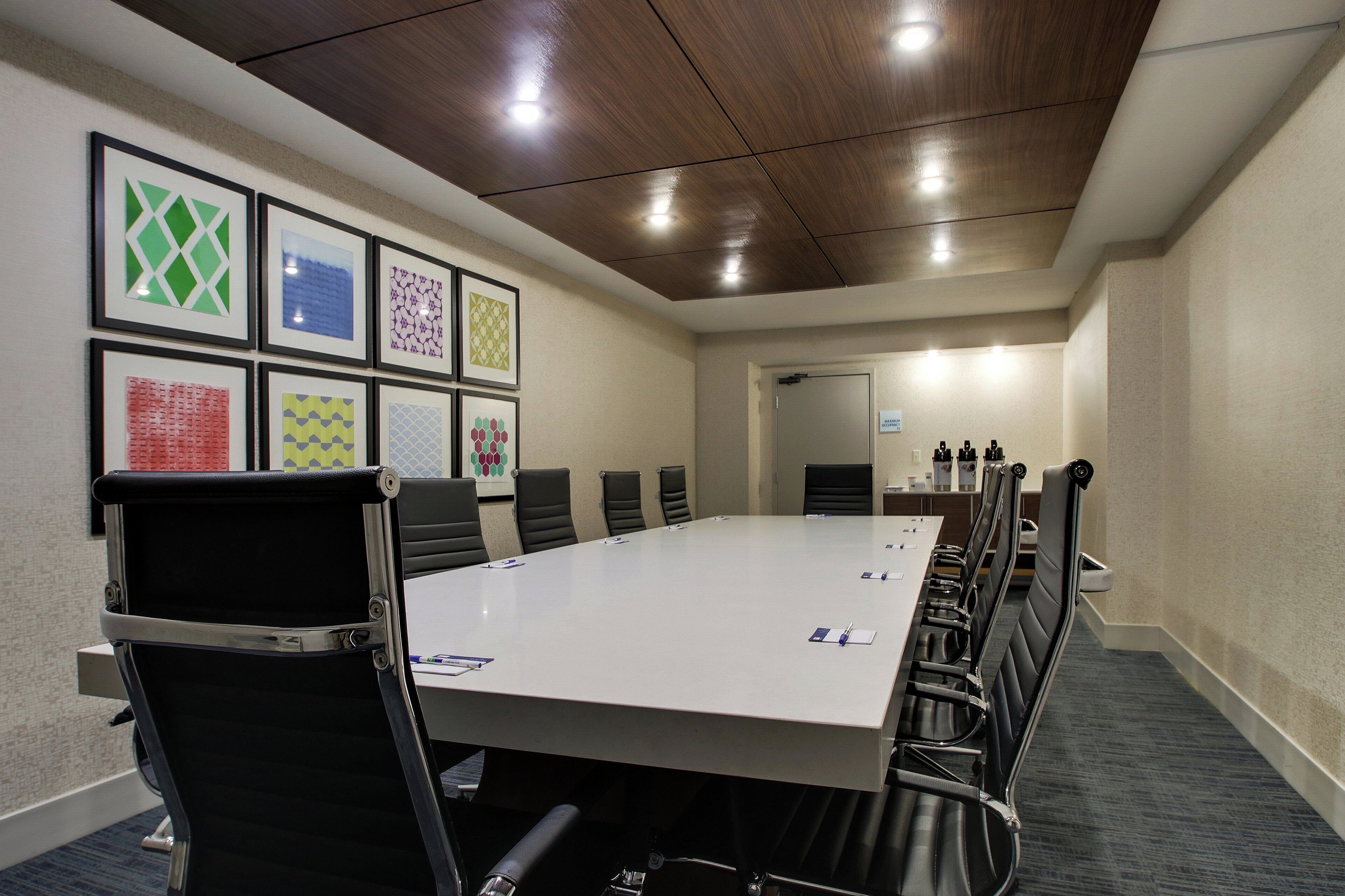 Un salón de conferencias con una mesa larga, sillas, cuadros en la pared y una puerta al fondo.