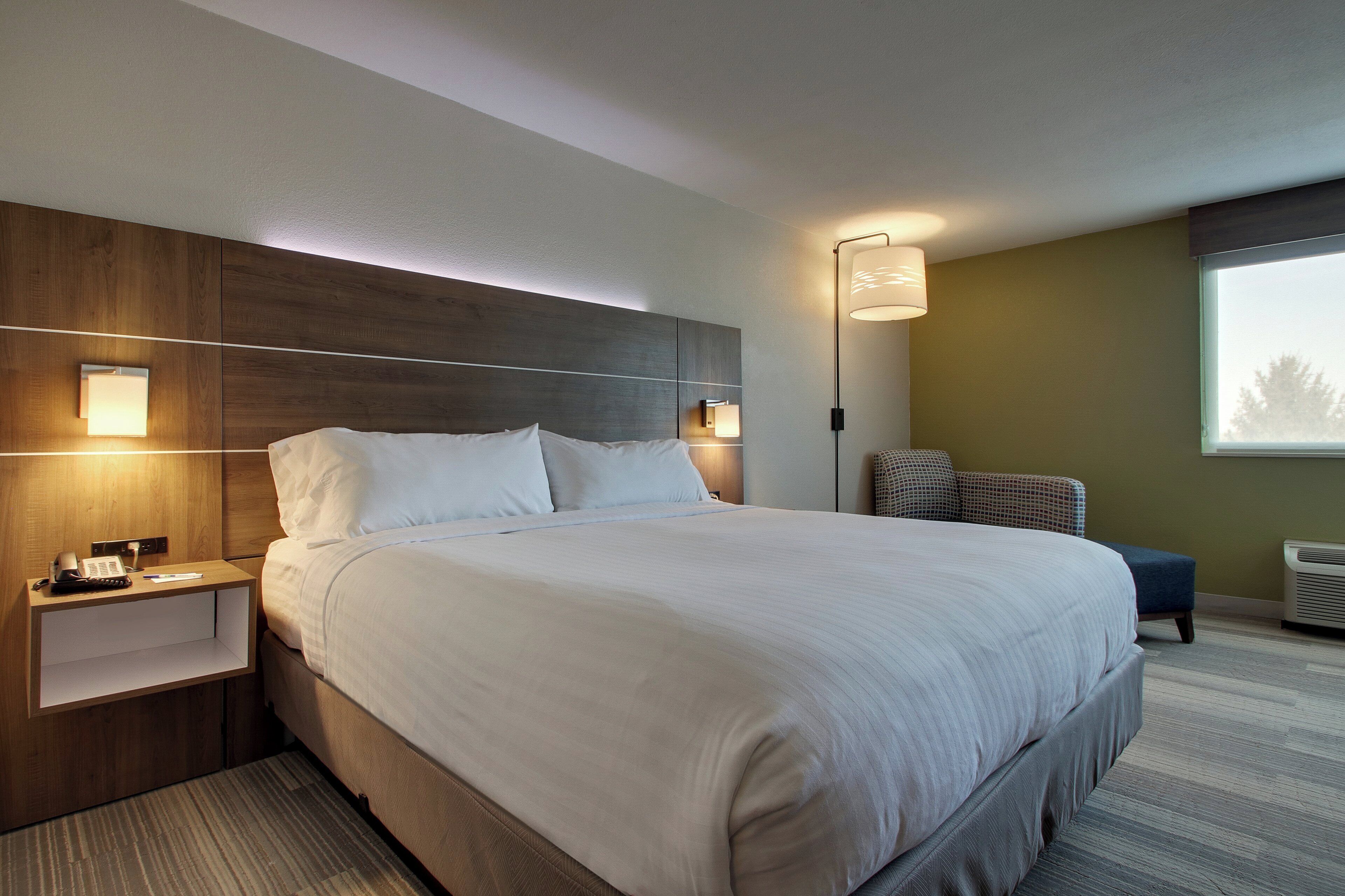 A hotel room with a large bed, bedside tables, a desk, a chair, a lamp, and a window.