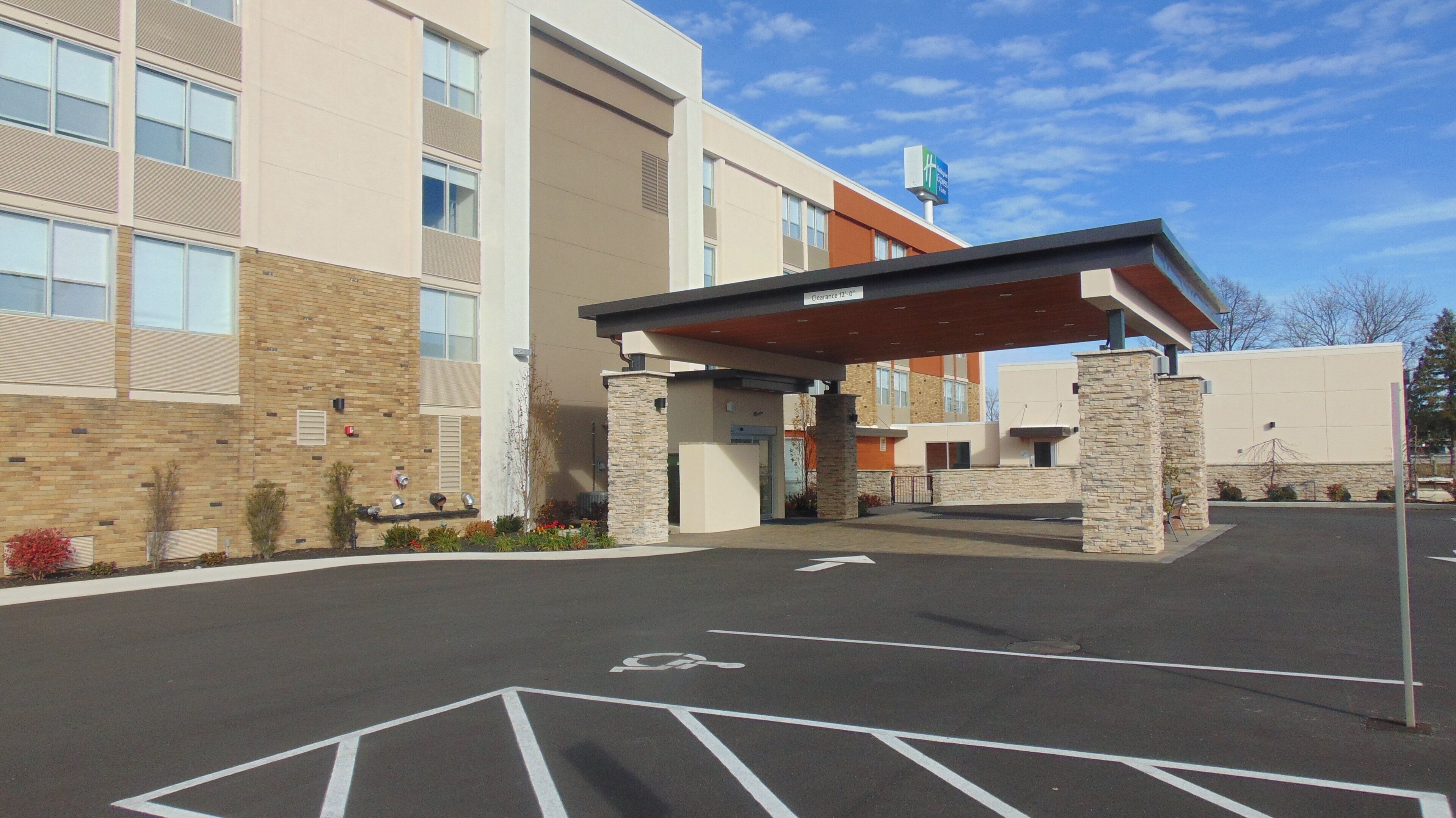 A hotel entrance with a covered walkway, a parking lot, and a clear sky.