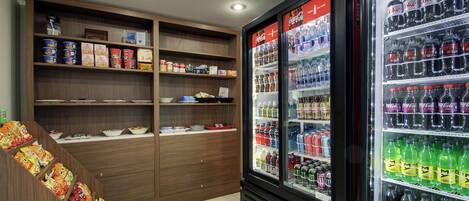 A kitchenette with a refrigerator stocked with beverages and a shelf with snacks.