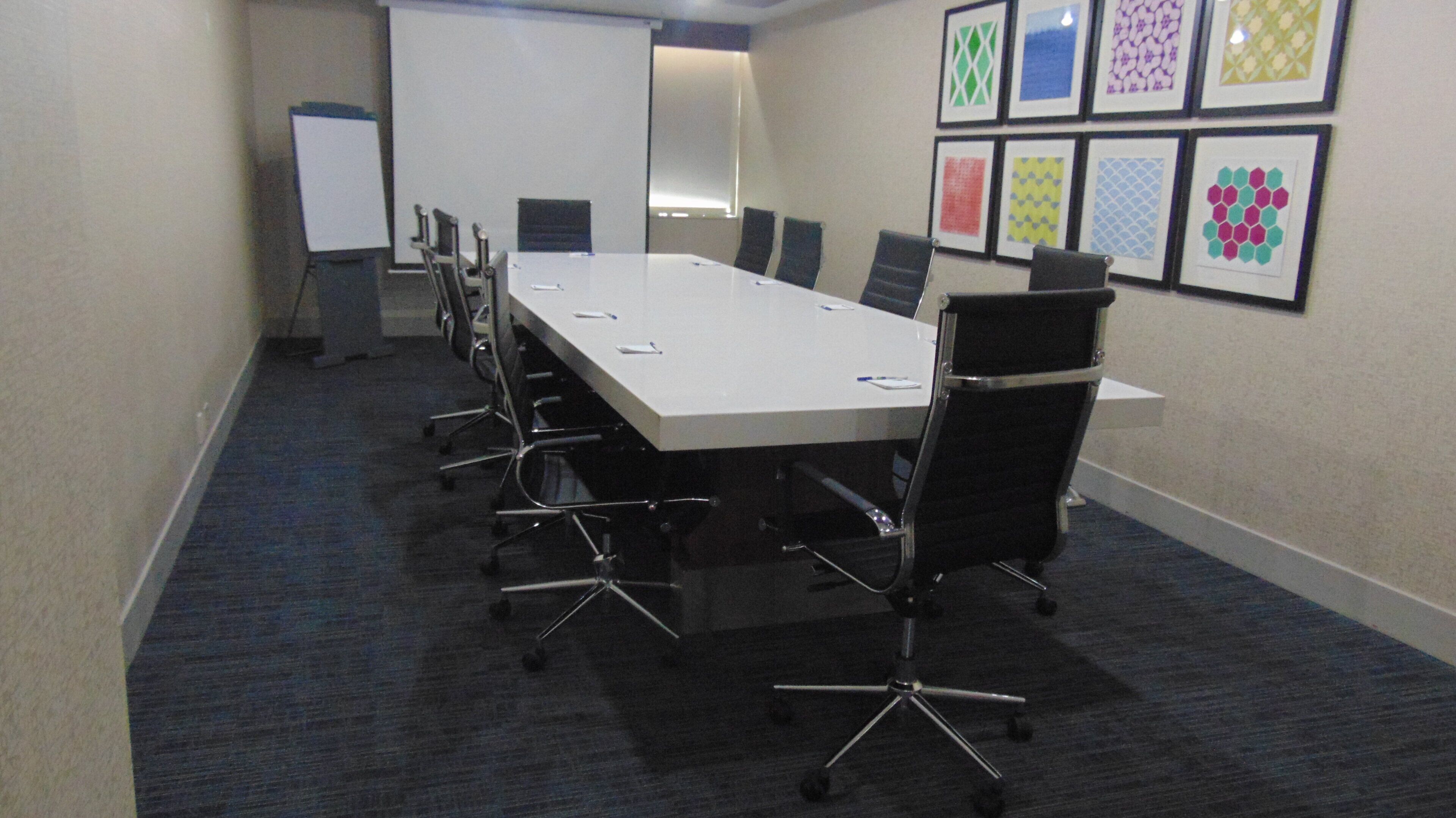 A conference room with a long table, chairs, a whiteboard, and framed artwork on the wall.