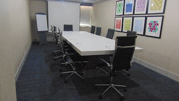 A conference room with a long table, chairs, a whiteboard, and framed artwork on the wall.