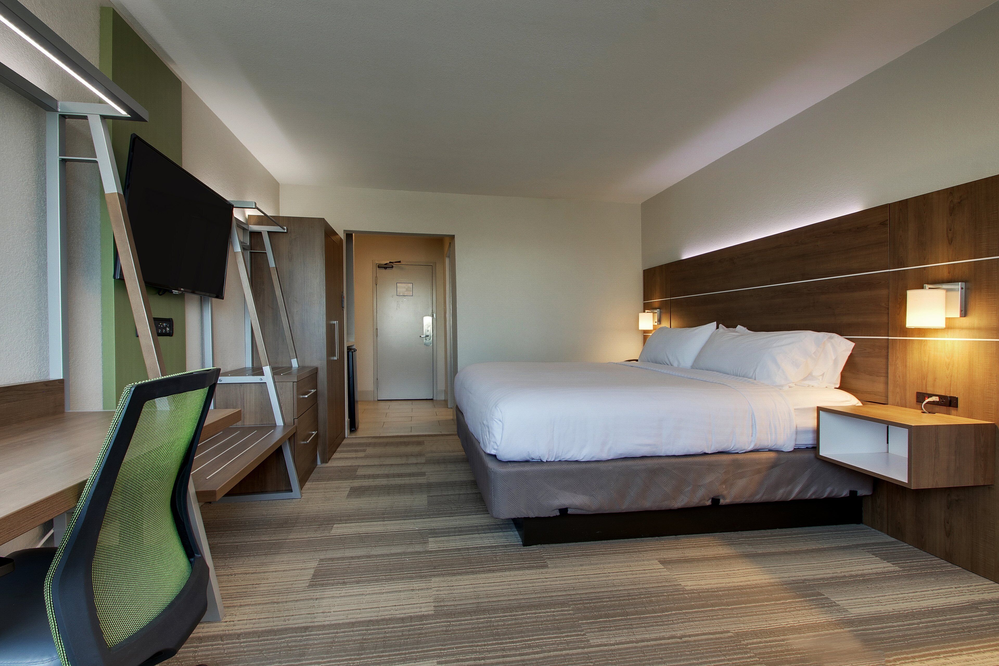 Een hotelkamer met een bed, een bureau, een stoel, een televisie en een nachtkastje met een lamp.