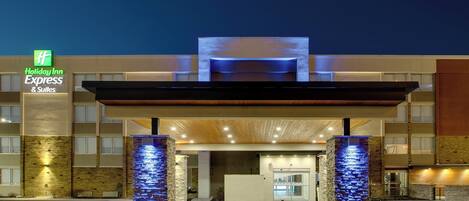A Holiday Inn Express & Suites hotel entrance with a modern design, featuring a prominent entrance canopy and illuminated pillars.