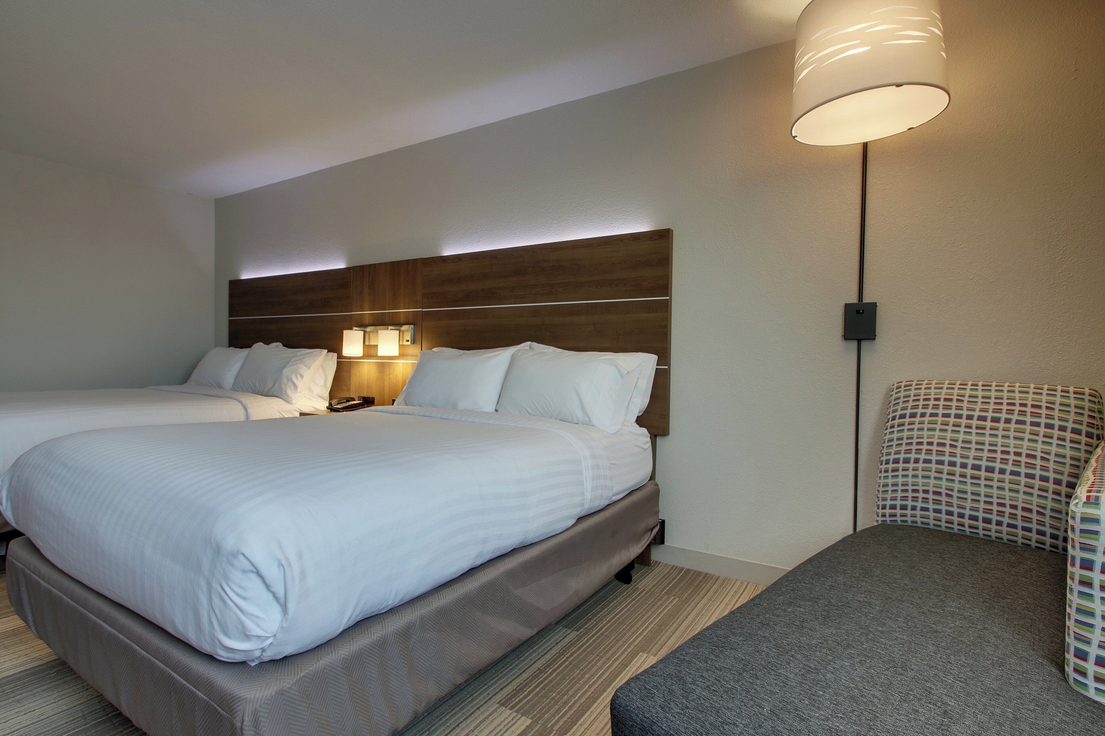 A hotel room with two beds, a nightstand, a lamp, and a patterned chair.