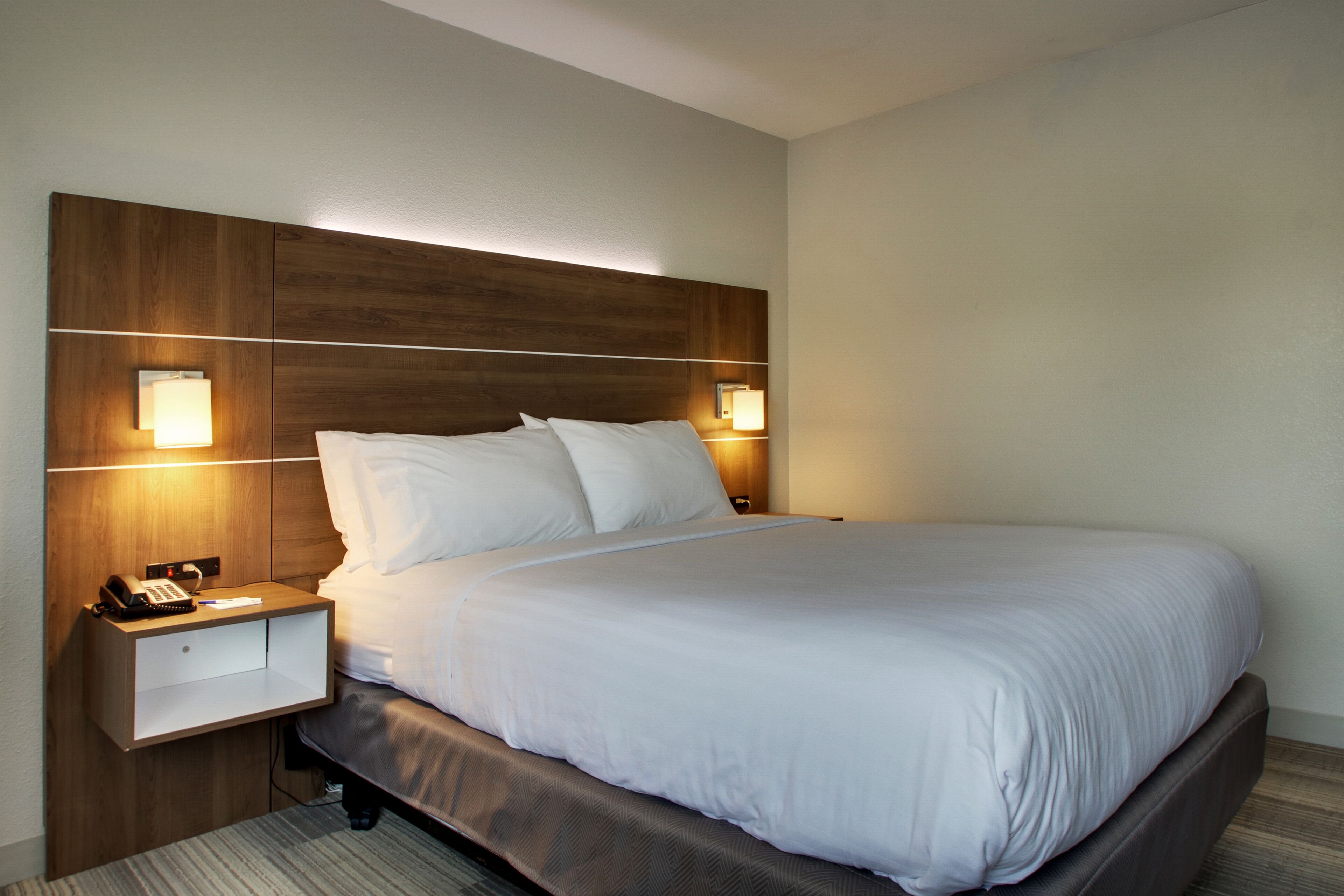 A hotel room with a large bed, two bedside tables, and wall-mounted lamps.