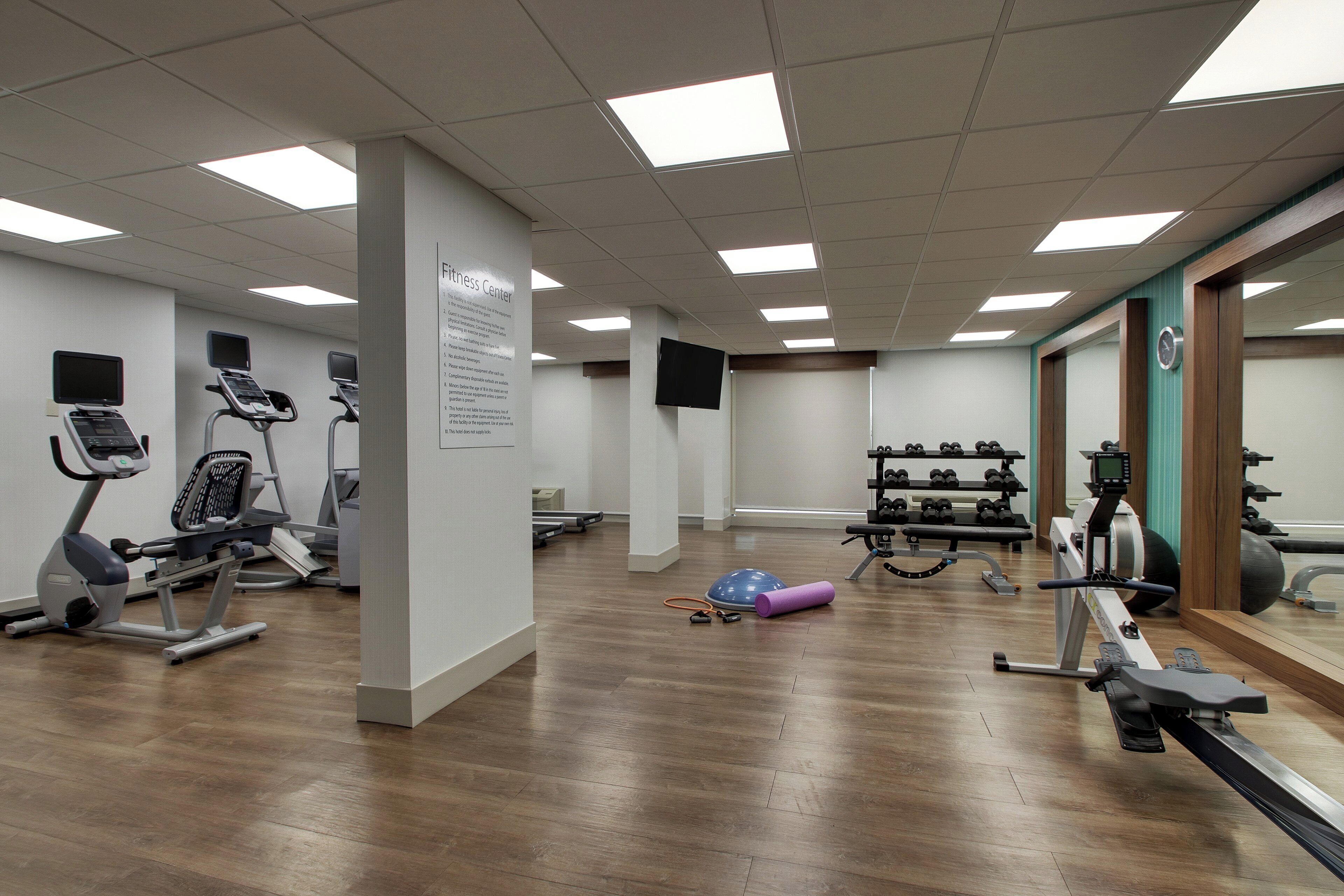 A fitness center with exercise equipment, a mirrored wall, and a bulletin board.