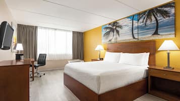 A hotel room with a bed, desk, chair, and a painting of palm trees on the wall.
