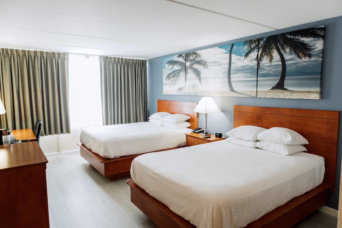 A hotel room with two beds, a desk, and a painting of a beach scene.
