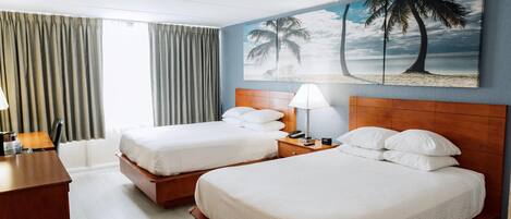 A hotel room with two beds, a desk, and a painting of a beach scene.