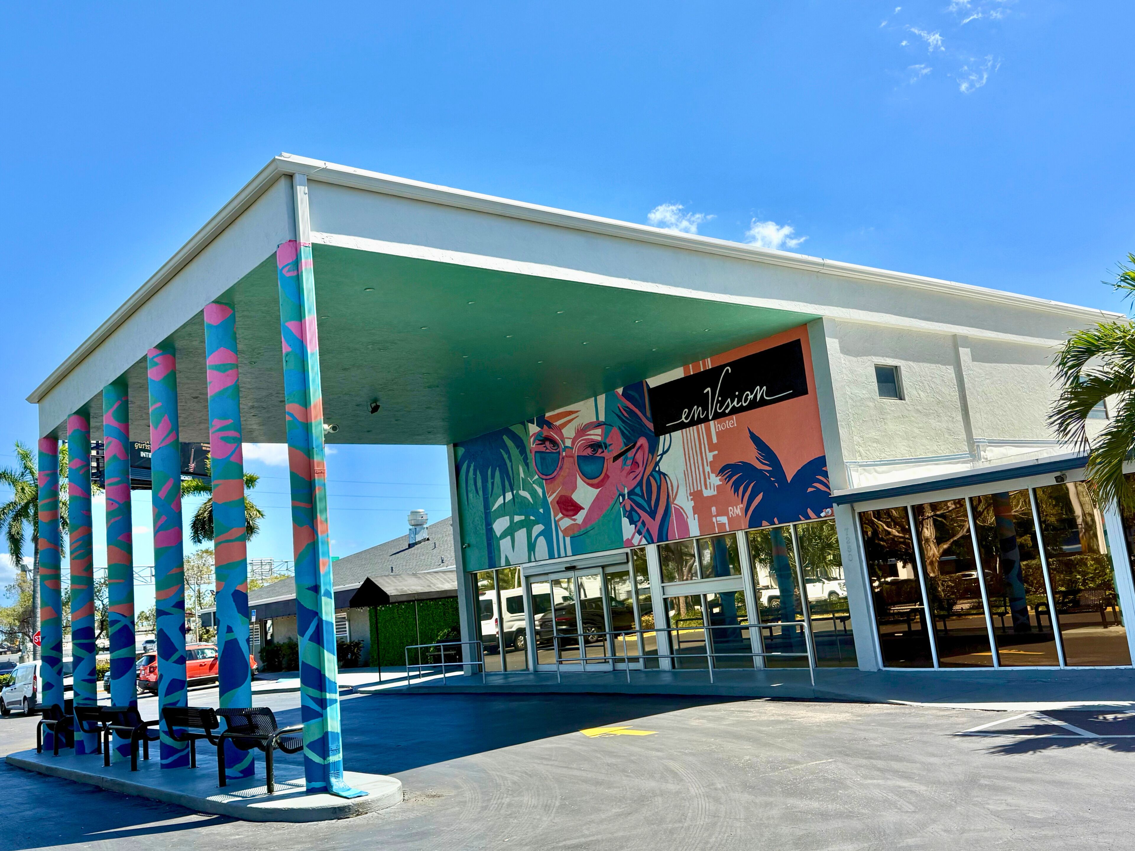Un hotel con un mural colorido, un acceso cubierto y un área de estacionamiento.