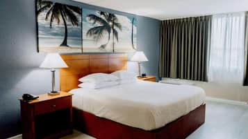A hotel room with a bed, two bedside tables, a nightstand, a headboard, and a large window with curtains.