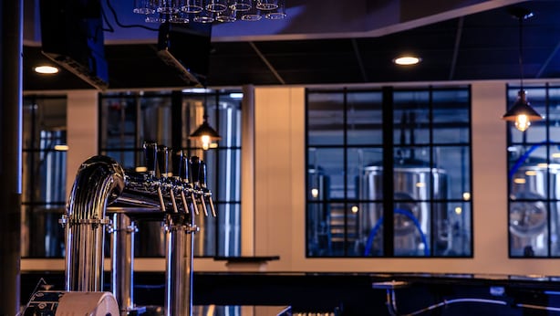 A bar area with a beer tap system, a counter, and industrial-style windows in the background. - enVision Hotel Miami International Airport (Miami)