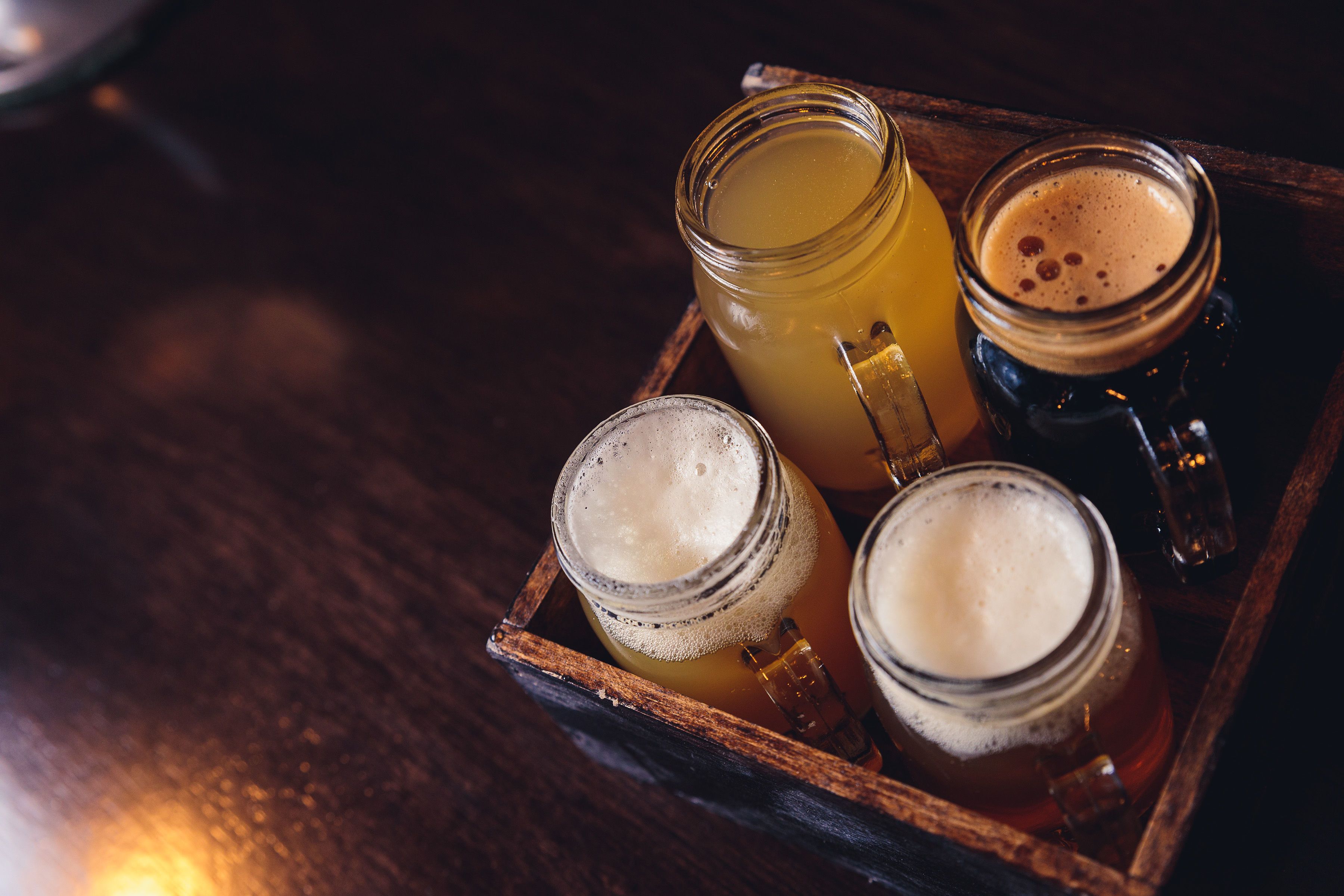 Una bandeja de madera con cuatro vasos de vidrio que contienen diferentes bebidas.