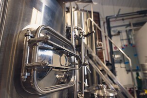 Primer plano de equipo de elaboración en acero inoxidable con válvulas y tuberías, indicando una planta de producción de cerveza.