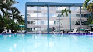 A swimming pool with lounge chairs and a building with large windows and palm trees in the background. - enVision Hotel Miami International Airport (Miami)