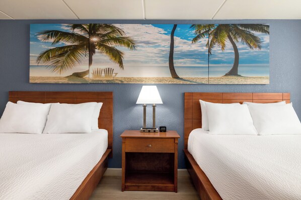A hotel room with two beds, a nightstand with a lamp, and a beach-themed wall mural.